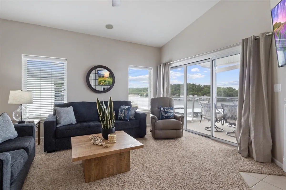 A serene seating area with a cozy arrangement, large glass sliding door, decorative mirror, and a coffee table with decorations. The sliding door visually connects the indoors to an outdoor screened porch, emphasizing the tranquil transition between spaces.
