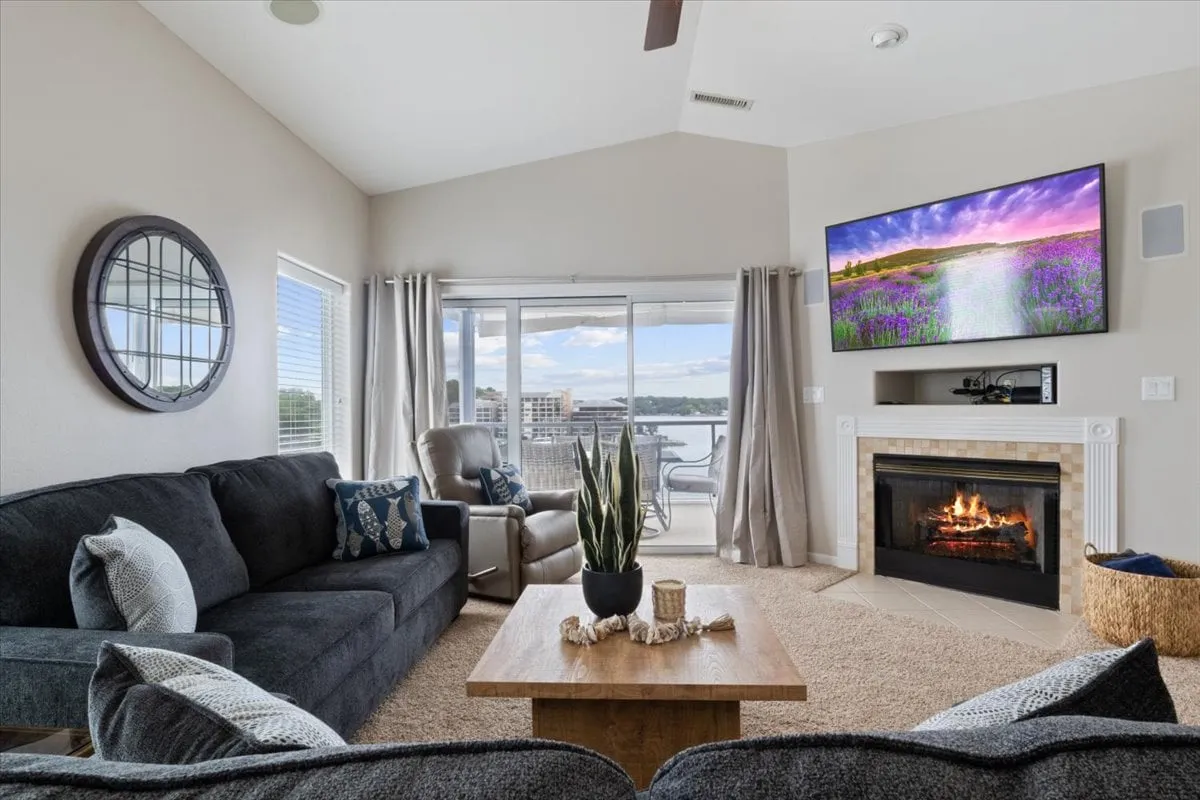 A cozy living room scene with a sofa, welcoming fireplace, television, and a window framing a scenic view. The space feels intimate and warm, ideal for relaxing evenings, lively conversations, or enjoying the sunset glow from indoors.
