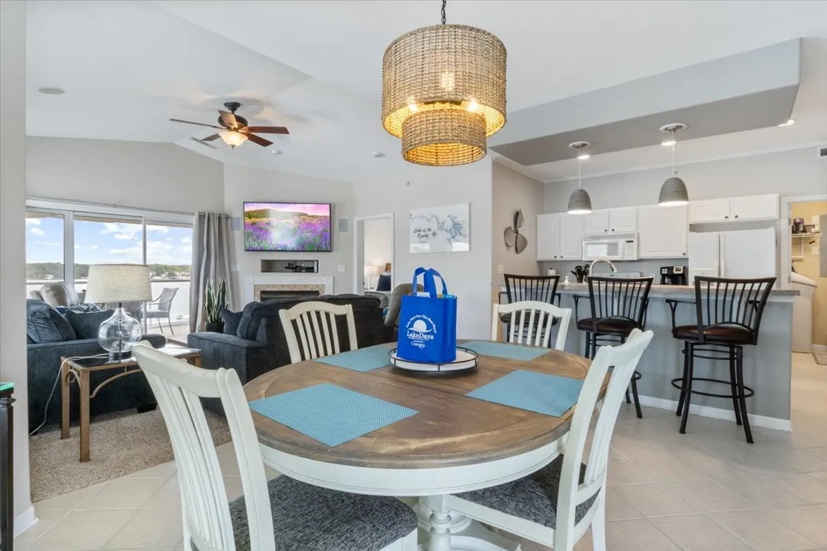 A modern dining area featuring a sturdy dining table, large windows letting in natural light, and a stylish light fixture overhead. The setup invites family meals, special occasions, and social gatherings, with lake scenery visible beyond.