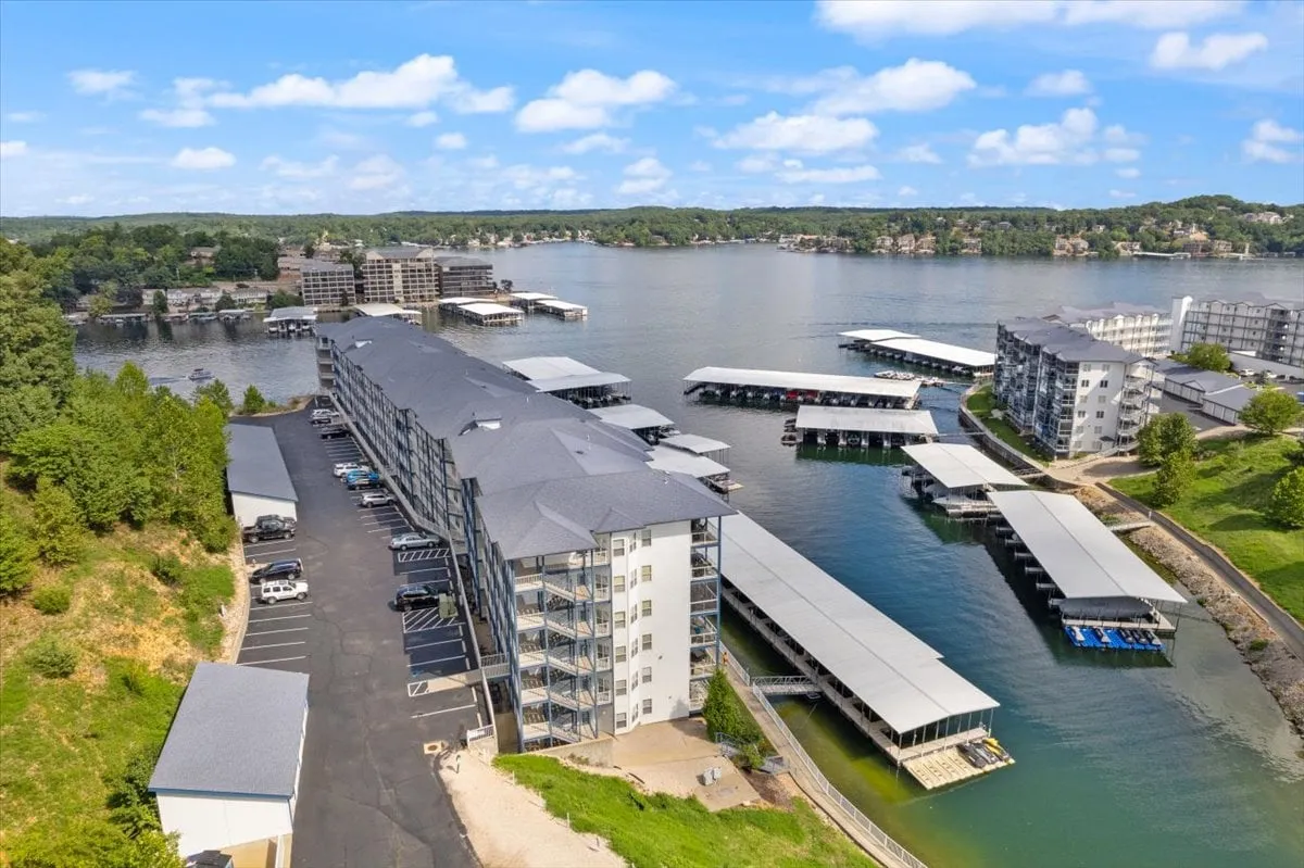 This waterfront scene shows boats in the marina, the surrounding greenery, and the building structure, all set against the tranquil lakeside. Activities like boating and fishing are visually suggested, with hints of sunset boat rides and picnics by the water.