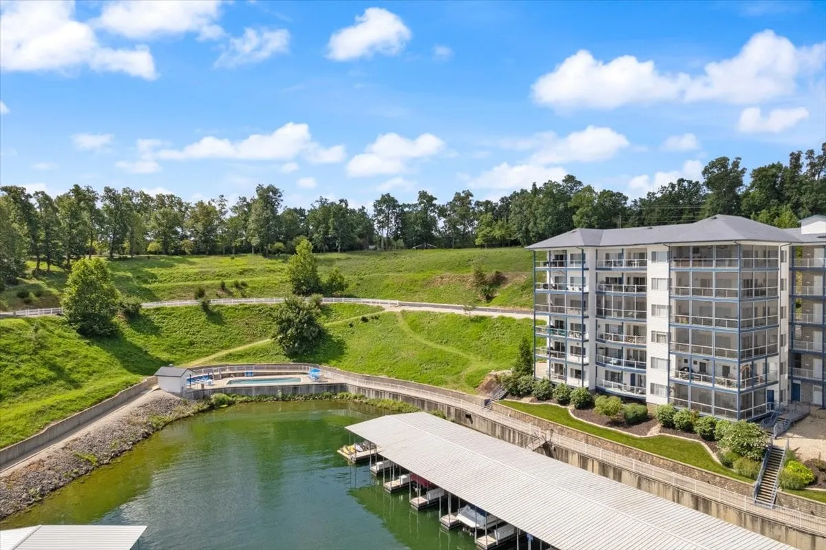 This exterior image features a waterfront area with boat docks extending into the lake, a residential building in the background, and lush green hills surrounding the scene. The docks are ideal for boating and fishing, directly aligning with the section's emphasis on lake access. The tranquil water and inviting dock area visually convey the property's prime location for water-based activities.