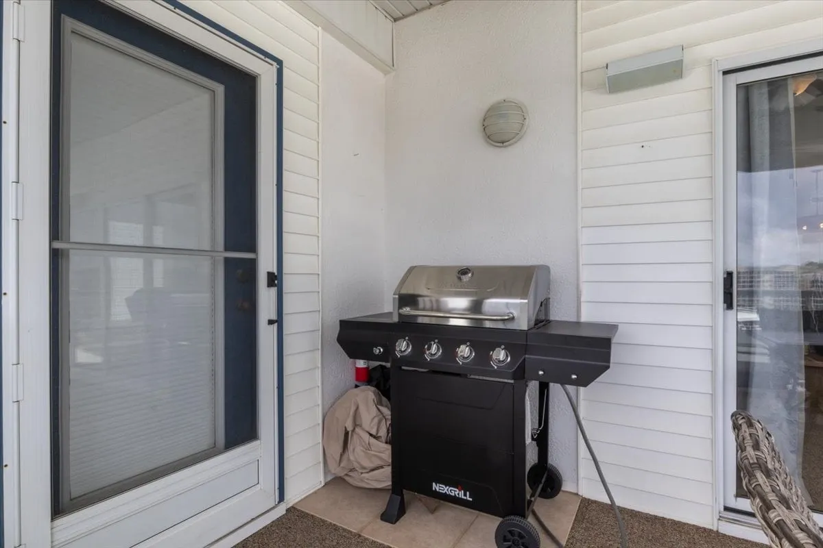 This exterior shot focuses on a grilling area with a modern grill, cozy seating, and a doorway leading inside. The ambiance is casual and welcoming, ideal for lakeside barbecues and gatherings with friends or family.
