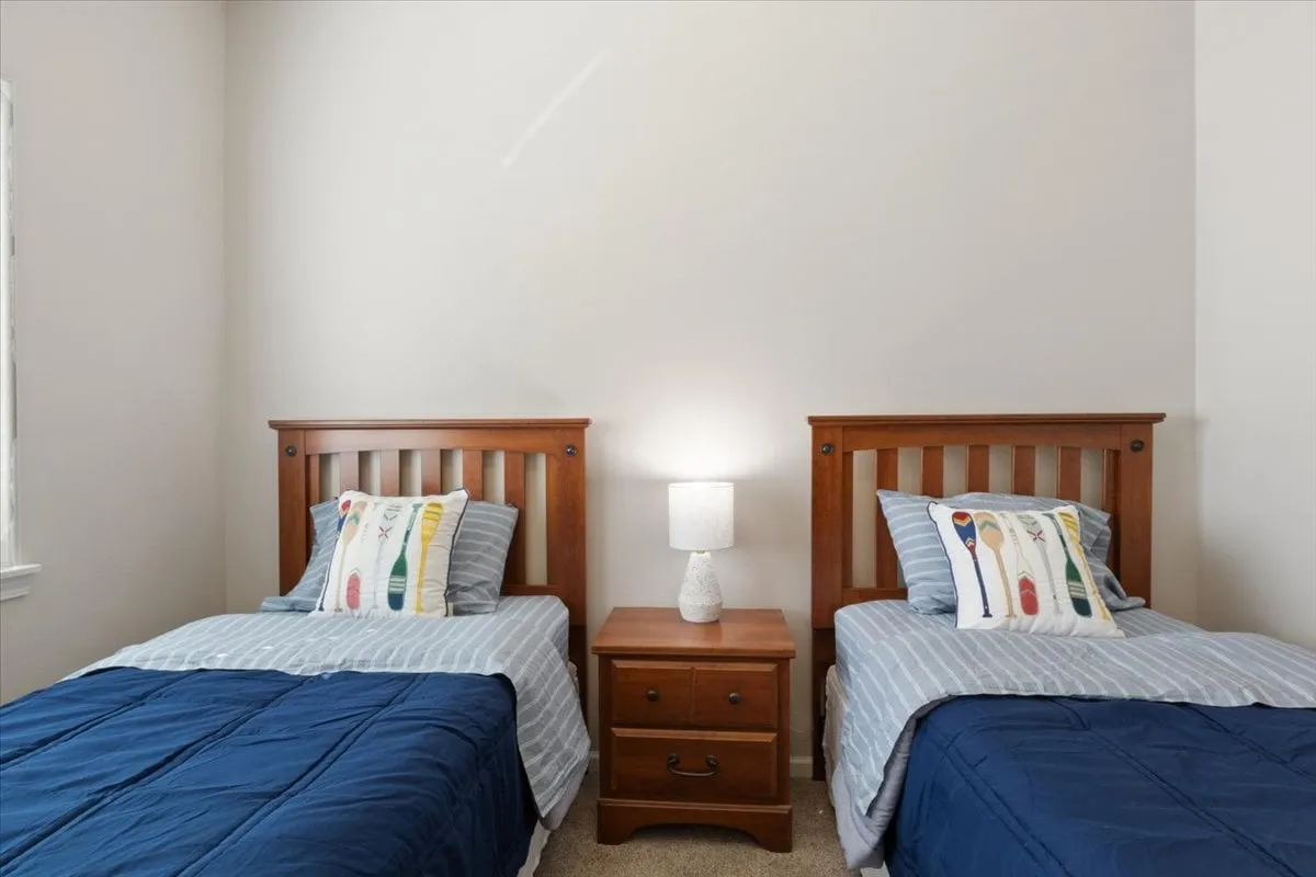 A cozy bedroom with twin beds, a nightstand, a table lamp, and decorative pillows. The space is inviting and ideal for kids or friends traveling together, with a warm, comfortable ambiance.