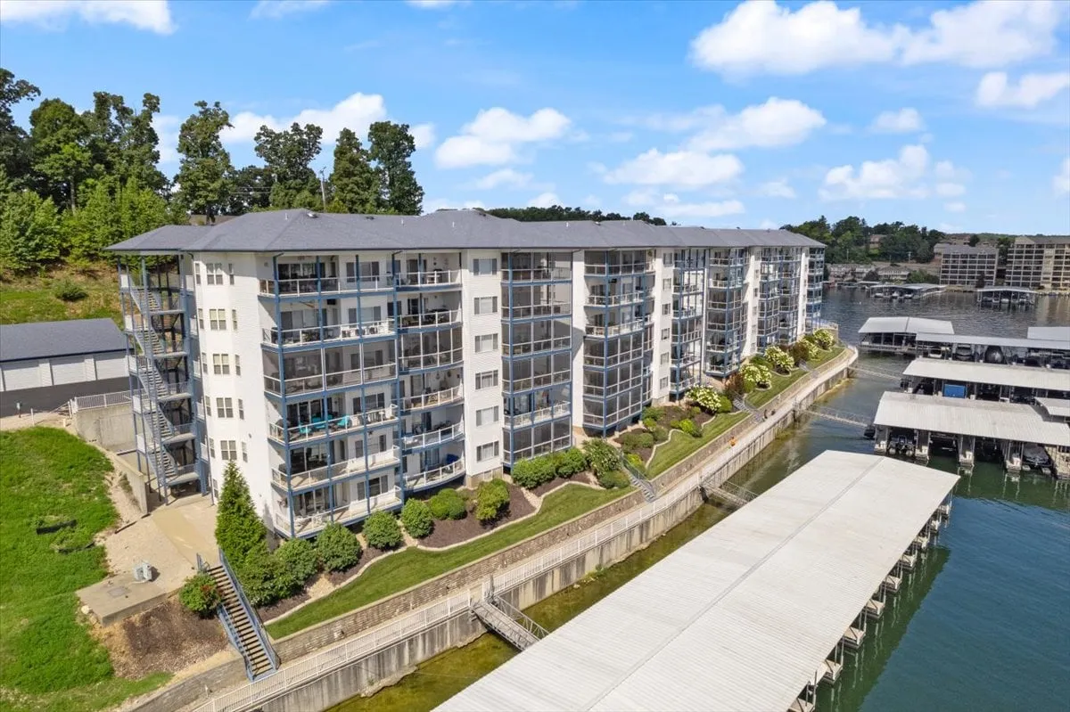 A tranquil exterior view of the modern apartment building with balconies overlooking the water, docks, and lush greenery in the surroundings. The image hints at the proximity to waterfront activities and vibrant community life.