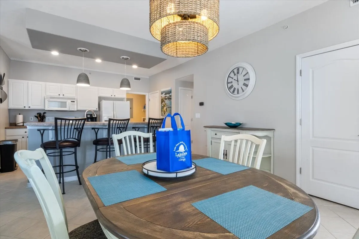 A cozy dining area is shown with a wooden dining table, elegant chandelier, and an adjoining kitchen area. The space is set for a meal, invoking the feeling of group gatherings and sharing stories over dinner, with the kitchen in full view for continuity.
